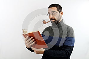 Intellectual bearded man with glasses with casual shirt on isolated white background holds a book in hand reading it with a pipe i