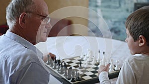 Intellectual games, old grandfather plays with his smart child playing board games of chess