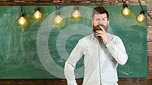 Intellectual task concept. Man with beard and mustache on thoughtful face stand in front of chalkboard. Bearded hipster