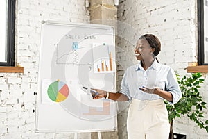 Intelligent african american woman stands near whiteboard with a graphs and charts on it
