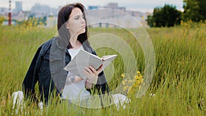 Intelligent caucasian woman sits on lawn outdoors reads book literature psychology bestseller educational encyclopedia