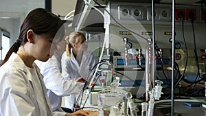 Intelligent Chinese girl working with reagent in test tube during chemical experiment with fellow students in university