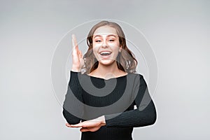 Intelligent enthusiastic young woman raises her hand up to attract attention and answer a question. Gray background