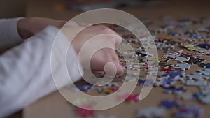 Intelligent girl wearing white shirt gathers puzzle closeup