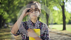 Intelligent nerd teenage boy adjusting eyeglasses looking at camera smiling. Front view portrait of confident smart