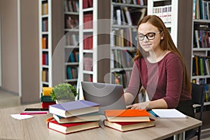 Intelligent redhead girl studying with laptop at library