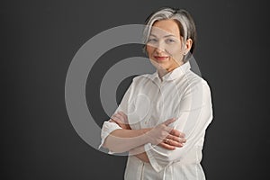 Intelligent silver-haired woman smiles with arms crossed. Pretty business woman looking at camera confidently. 