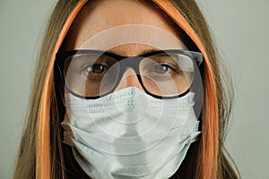 Intelligent woman in eyeglasses wearing medical mask, close-up portrait with focus on eyes.