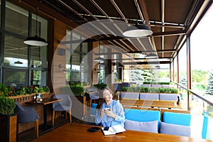 Intellingent student in sitting at cafe with notebook and smartphone, drinking coffee.