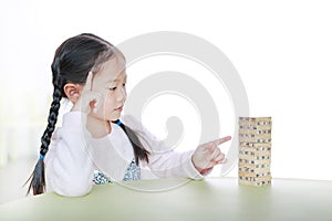 Intend little Asian child girl thinking to playing wood blocks tower game for Brain and Physical development skill in a classroom