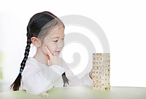 Intend little Asian child girl thinking to playing wood blocks tower game for Brain and Physical development skill in a classroom