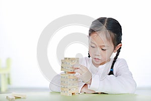 Intend little Asian child girl thinking to playing wood blocks tower game for Brain and Physical development skill in a classroom