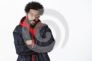 Intense attractive african american guy with beard and afro hairstyle in denim jacket over hoodie and glasses crossing