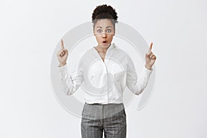 Intense shocked and surprised attractive african businesswoman in suit, pointing up while gasping and staring with