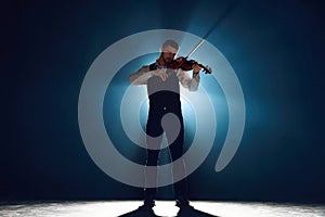 Intense violin recital with musician standing on stage with backlights against darkness with smoke. Instrumental classic