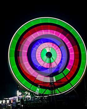 Intentional camera movement, slow shutter blur image of giant Ferris wheel illuminated and spinning at night in a fun fair