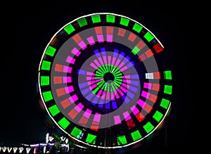 Intentional camera movement, slow shutter blur image of giant Ferris wheel illuminated and spinning at night in a fun fair