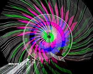 Intentional camera movement, slow shutter Zoom blur image of giant Ferris wheel illuminated and spinning at night in a fun fair