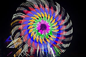 Intentional camera movement, slow shutter Zoom blur image of giant Ferris wheel illuminated and spinning at night in a funfair