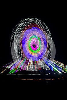 Intentional camera movement, slow shutter Zoom blur image of giant Ferris wheel illuminated and spinning at night in a funfair