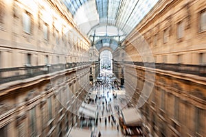 Intentionally blurred abstract view of Galleria Vittorio Emanuele II with people shopping in Milan, Italy.
