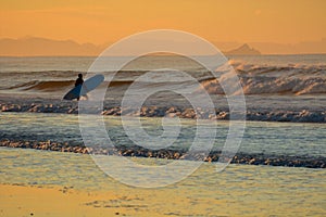 Intentionally blurry background image - oil painting effect. Beautiful seascape at sunset and a surfer entering the sea.