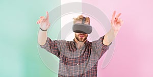 Interaction in virtual reality with digital surface. Man unshaven guy with VR glasses, pink background. Hipster use