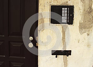 Intercom device with numbers on old breaking plaster wall near black entrance door