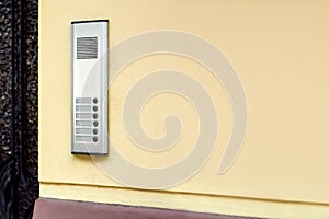 Intercom with a microphone and call buttons mounted on a yellow wall.