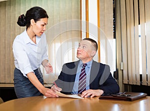 Businessman signing papers brought by female partner in meeting room