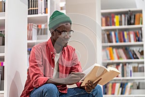 Interested African American student guy reading book in university library, studying for exam.