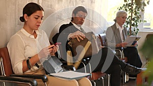 Interested attractive young woman in casual outfit sitting on chair in office corridor, waiting for job interview