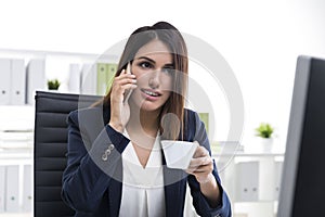 Interested brown haired businesswoman with a smartphone and a cu