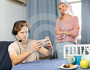 Teen boy playing game on phone against background of frustrated mother