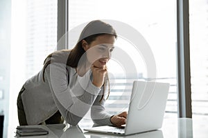 Interested female worker standing near desk looking on laptop screen