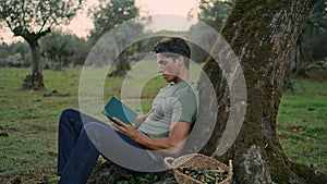 Interested gardener reading storybook evening nature closeup. Man leaning tree