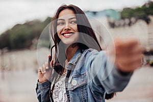 Interested glamorous woman in oversized denim jacket makes selfie. Gorgeous brunette girl takes pictures of herself while walking