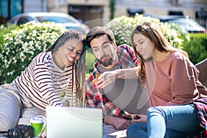 Interested guy and smiling girls on picnic in front of laptop