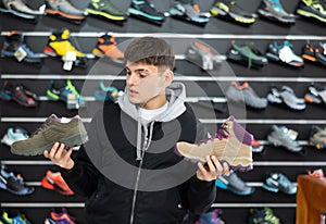 Interested male athlete chooses sports winter shoes for hiking in sports store