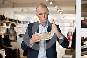 Interested man checking softness of sole of moccasins in shoe store