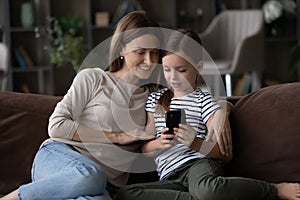 Interested mom watch tween daughter play game on modern smartphone