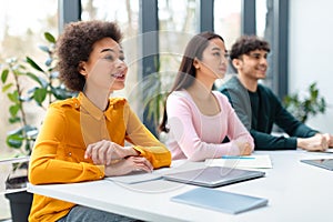 Interested positive multiracial students listening lecture, groupmates sitting at table in classroom and looking aside