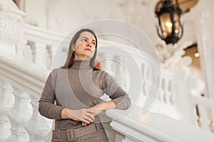 Interested woman standing near stucco railings on stairs in antique palace