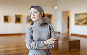 Interested woman visiting exhibition of paintings in art museum