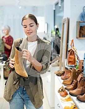 Interested young woman choosing comfortable fall footwear in shoe store