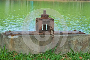 An interesting, old and rustic water gateway that allows the flow or damming of water to and from a large lush Thai park lake.