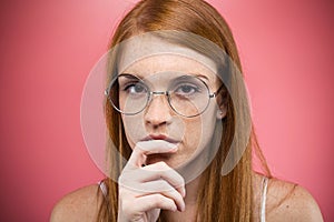 Interesting young woman with eyeglasses thinking and looking at camera over pink backgound