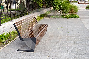 Interestingly designed street bench stands on the asphalt next to a metal fence photo