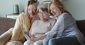 Intergenerational family 3 females using smartphone on sofa having fun