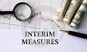 INTERIM MEASURES - words on a white sheet against the background of a chart, magnifying glass and banknotes photo